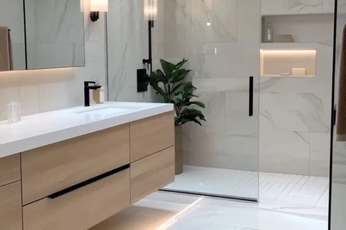 Modern Marble and Wood Bathroom A modern, brightly lit bathroom featuring white marble tiles on the walls and floor, a large wooden vanity with a white countertop and double sinks, a spacious glass-enclosed walk-in shower with a black rainfall showerhead, and a skylight.